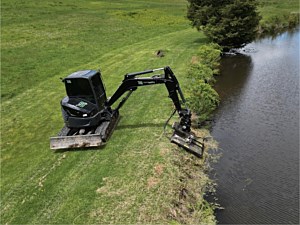 Excavator with brush mower being used to mow a pond bank in Glenmoore